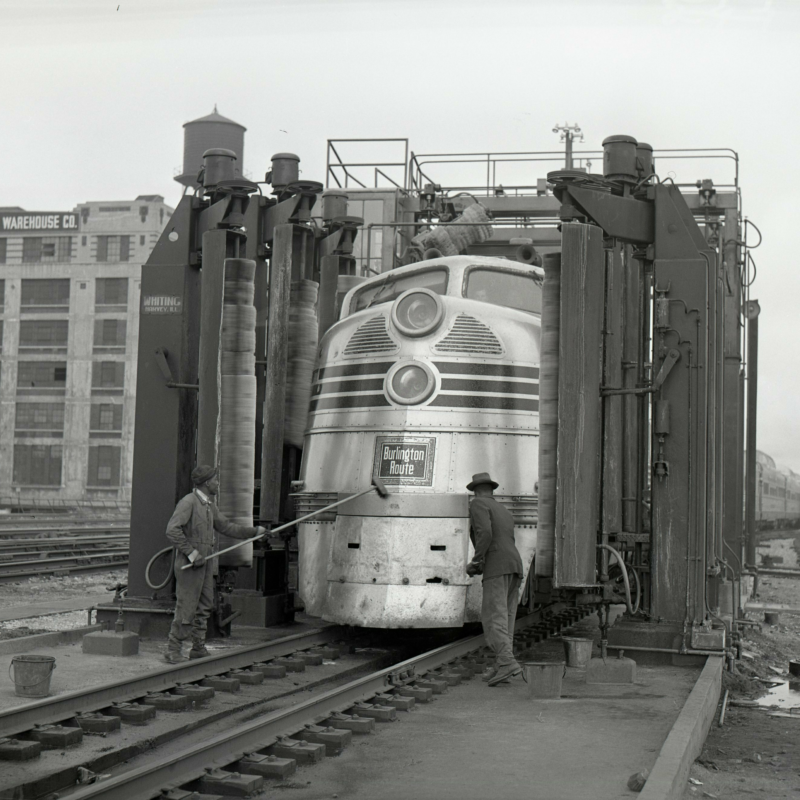 A large metal train being cleaned by two workers from the CB&Q railroad company