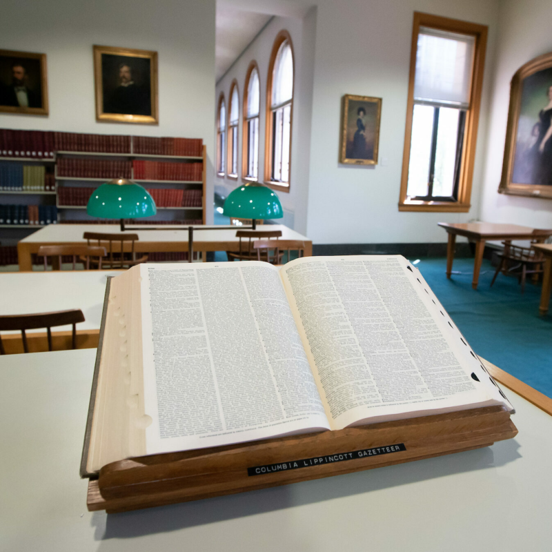 A dictionary lies open on top of a shelf of books.