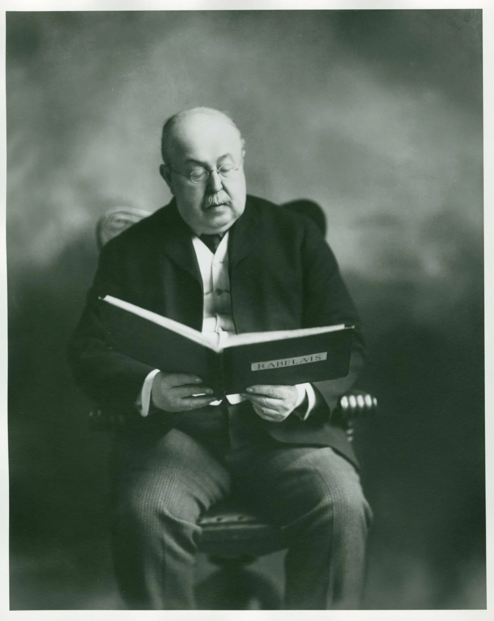 An older man sits in a chair reading.