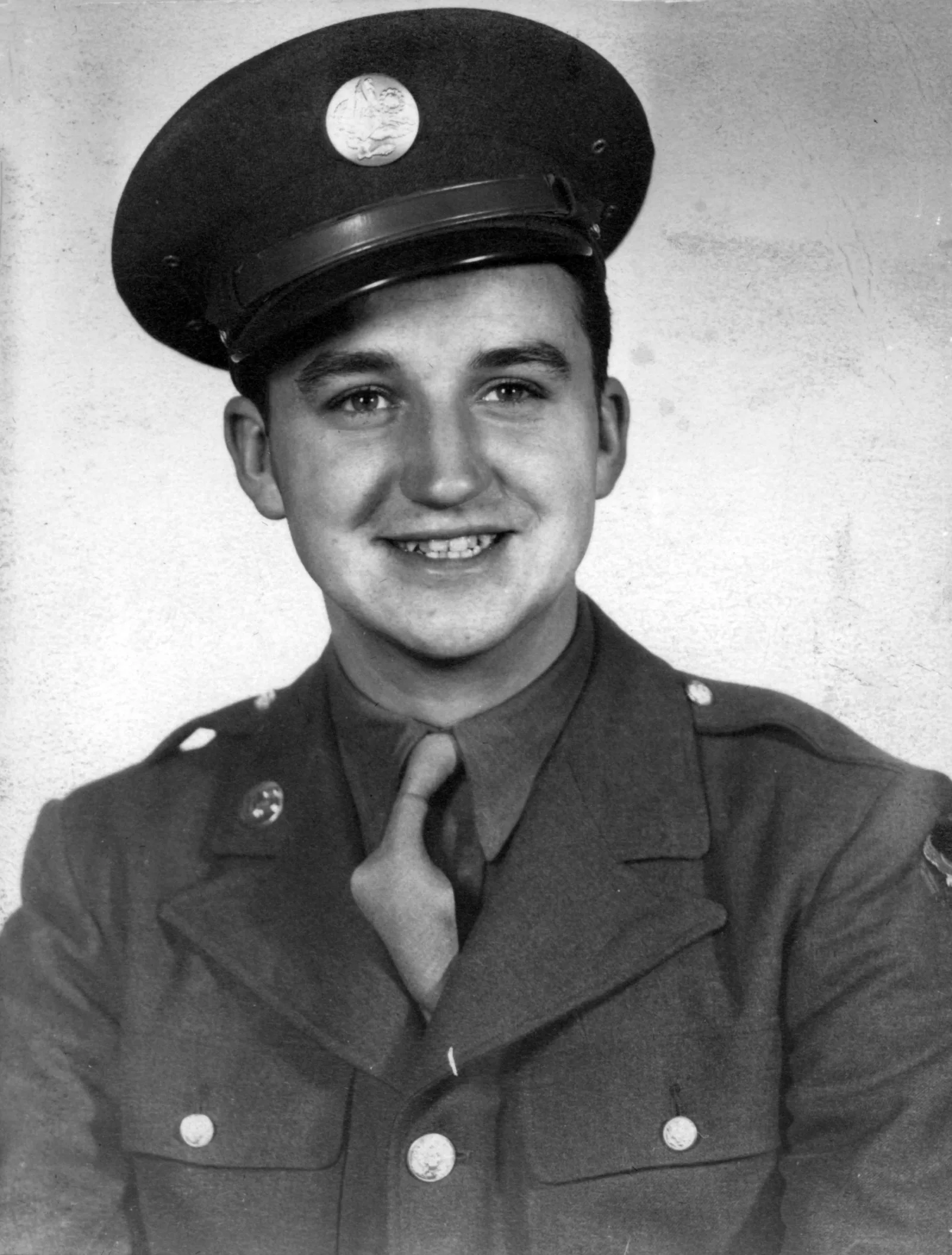A young man smiles in military uniform while serving overseas during World War II