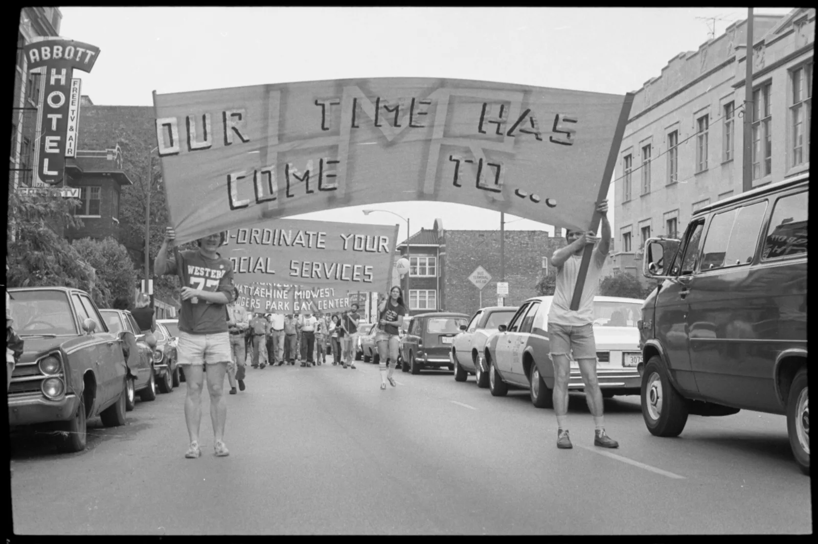 Two people holding up a sign in a parade. The sign reads, "Our time has come to..."