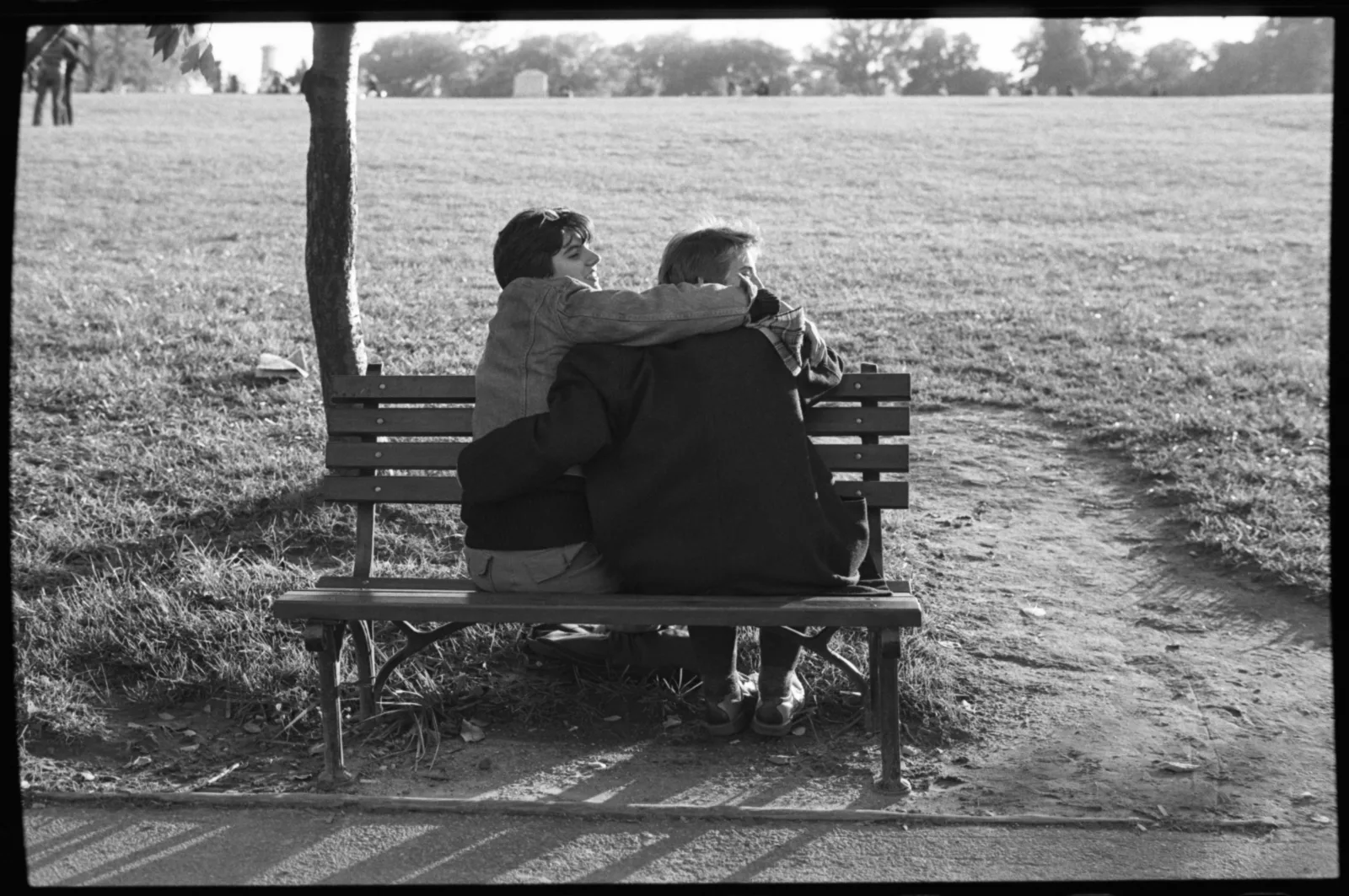 Two people sit and embrace on a park bench.