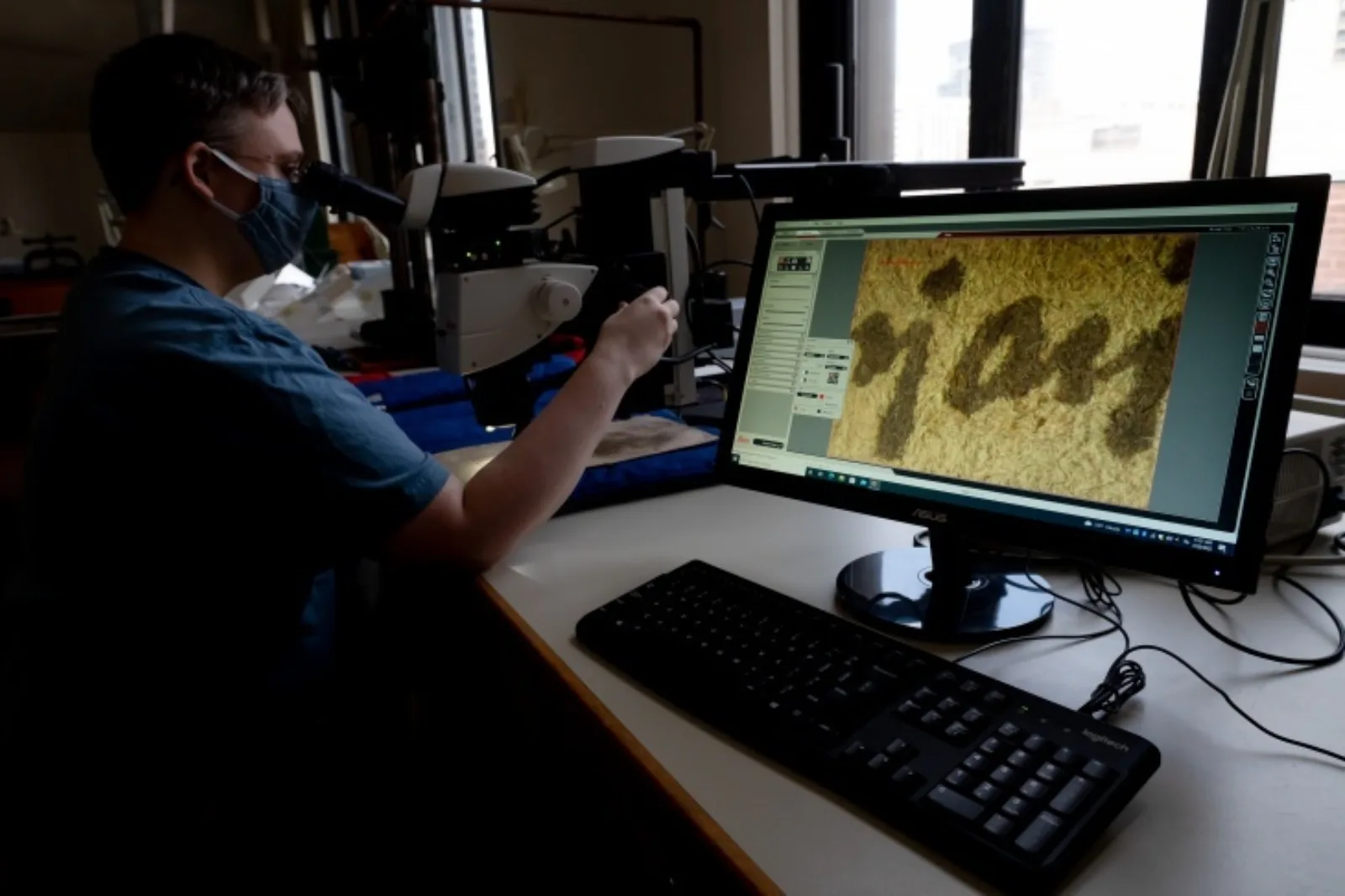 Leith is looking at Ayer 1485 through a powerful microscope. On the right is a computer monitor that displays the view of the microscope.