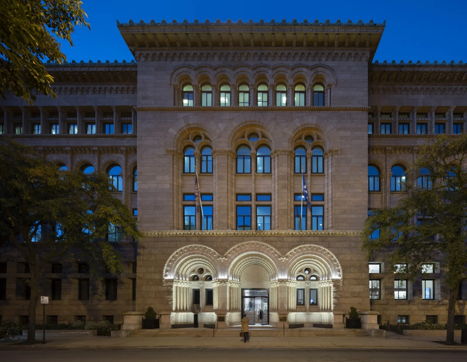 The front of the Newberry at dusk. Lights highlight the three rounded arches of the front entrance.