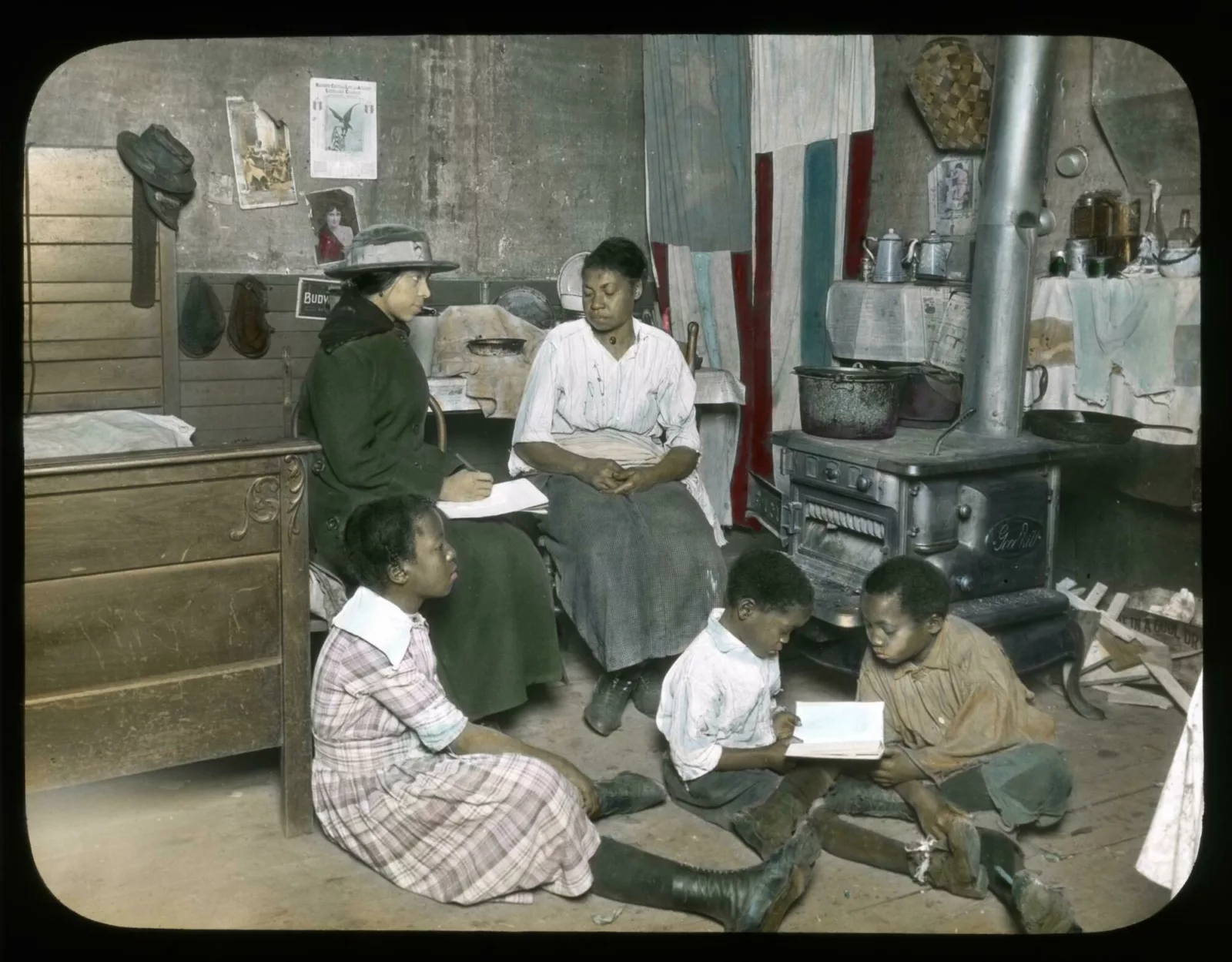 A social service worker sits on a chair next to a woman. Three children sit on the floor and look at a book together.