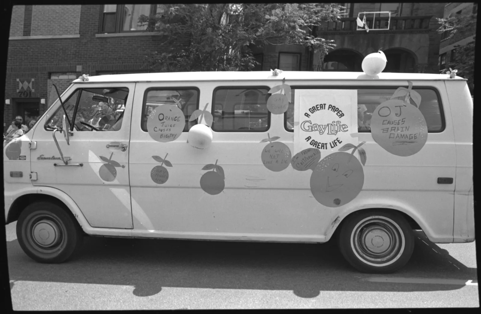 A large van decorated with oranges. A sign on the van reads "A Gay Life: A Great Paper, A Great Life."