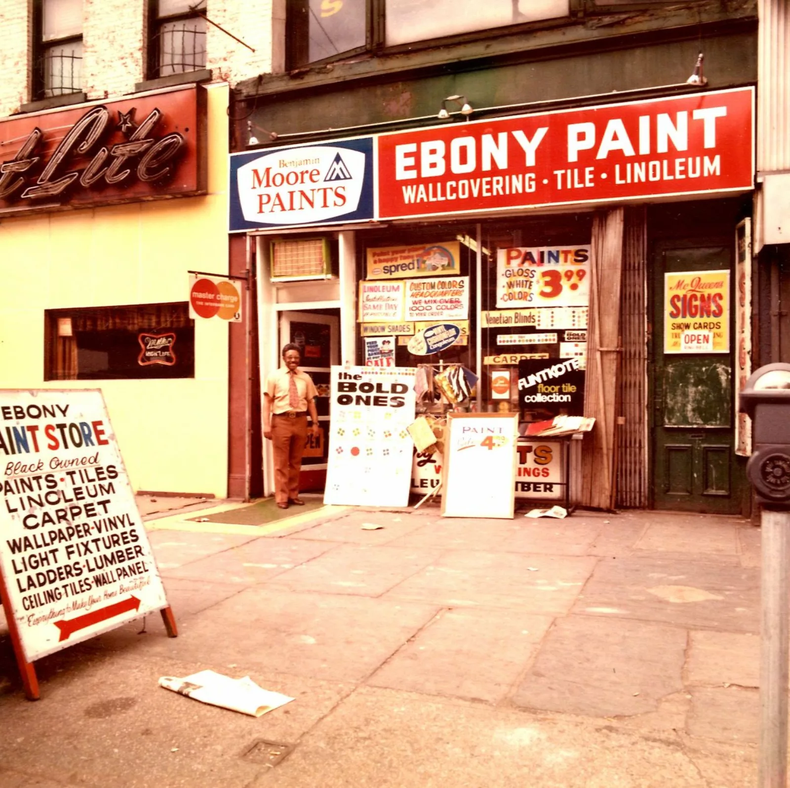 Above the Ebony Paint storefront is a red sign with white letters: Ebony Paint: Wallcovering, Tile, Linoleum