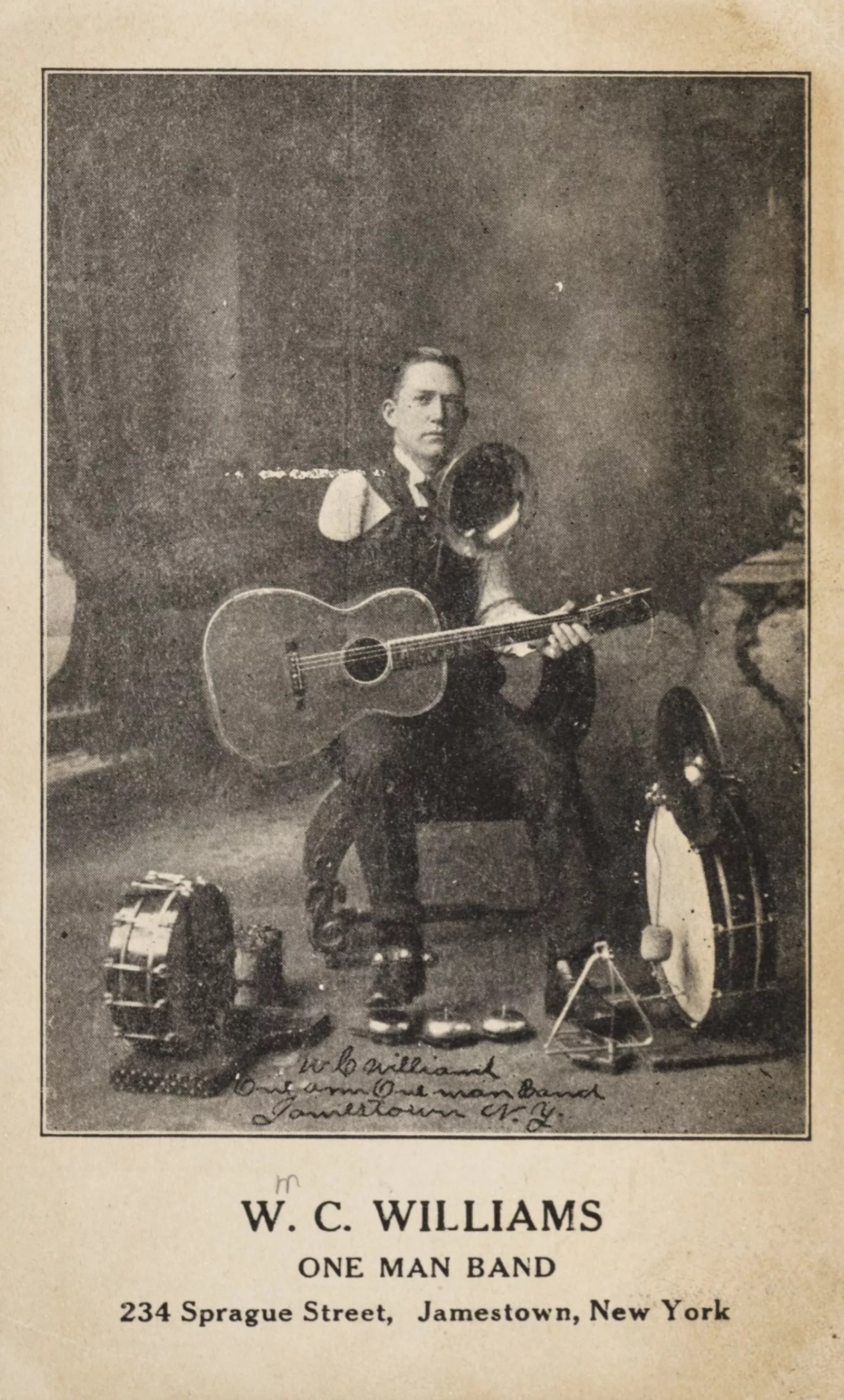 Williams seated with his many instruments, including a guitar, trombone, and multiple drums.