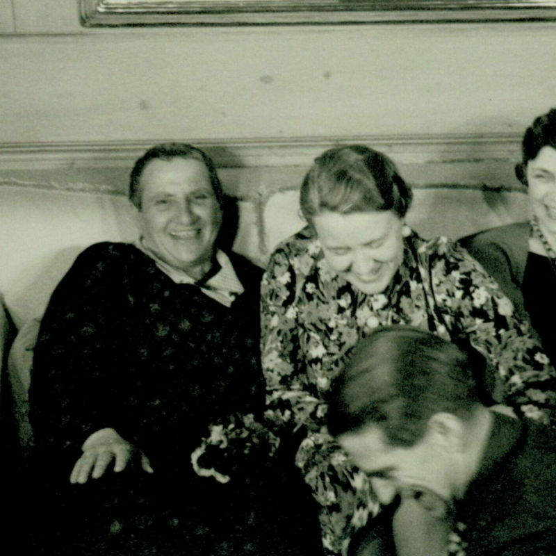 Four women sit on a couch laughing.