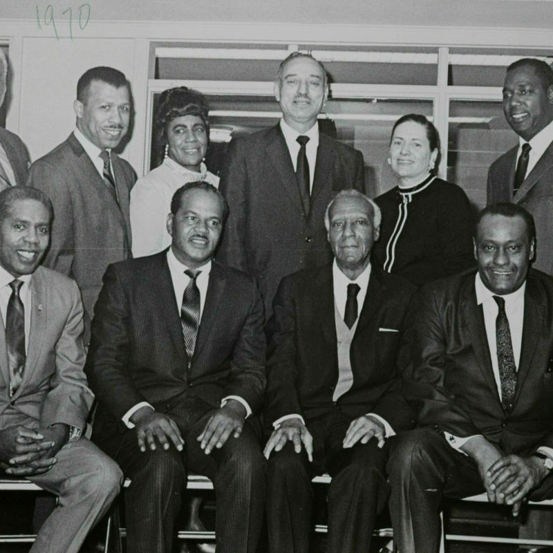 Members of the NAACP dressed in formal business attire pose for a picture. The front row is seated and the back row is standing behind them.