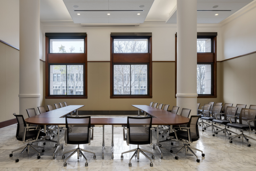Baskes Boardroom set up in a conference seating style. Rolling chairs are placed around a U-shaped table. The room has three large windows and two pillars.