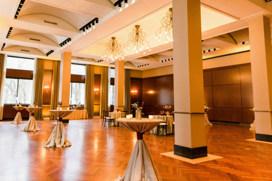 High-boy tables are set up in a large banquet hall with a polished wood floor.